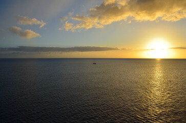 Golden sunset at sea, sailing boat on horizon, reflections of sunrays, sunset sky with clouds