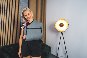 Young Caucasian woman with broken arm and wearing a sling at home and smiling, medium shot. High...