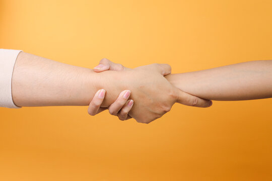 Two hands grabbing each other wrist to helping over yellow background