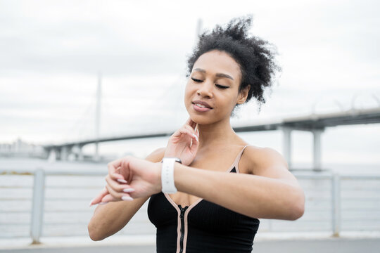 Fitness-focused woman checks her smartwatch during an outdoor exercise near a bridge.
