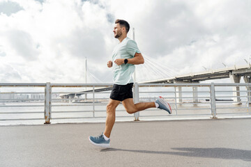 Man jogging on a sunny day with a bridge in the background, focused on his fitness goals.