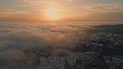 Golden sunset illuminating cloudy town at evening. Aerial sun over light clouds