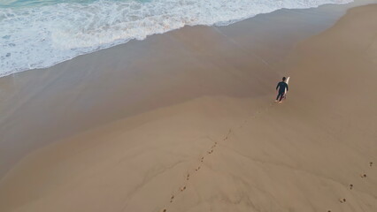 Man surfer leaving footprints walking beach. Drone surfboarder stepping wet sand