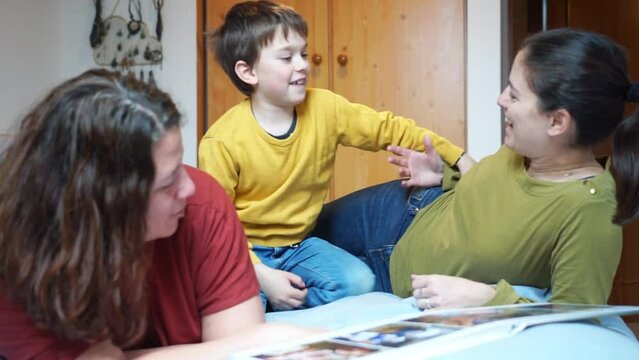 LGTBQIA+ family of two mothers and their son tickling each other on the bed in the bedroom