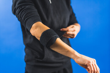 a person applying an elbow brace on an injured hand, blue background. High quality photo