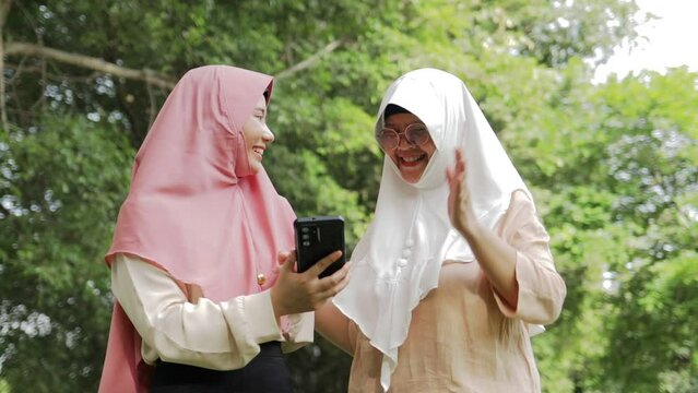 Two Islamic women, mother and daughter, are in the outdoor garden. Smiling happily, holding a smartphone and taking pictures together. family concept