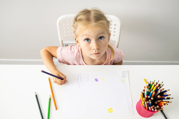 A child blonde girl draws with colored pencils sitting at the table. Top view, flat lay