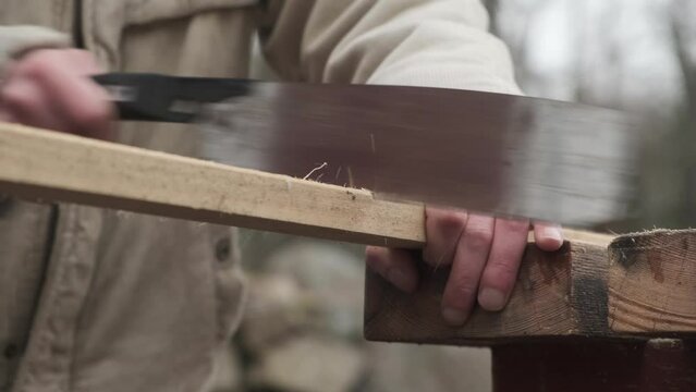 Closeup of a man using a hand saw to cut wood in an outside Setting