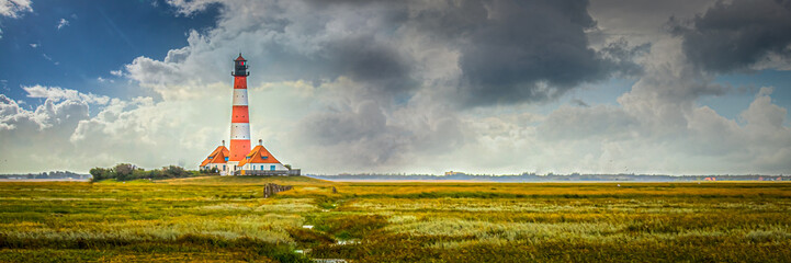 Fototapeta na wymiar Picturesque Lighthouse Amidst Green Fields Under Cloudy Sky