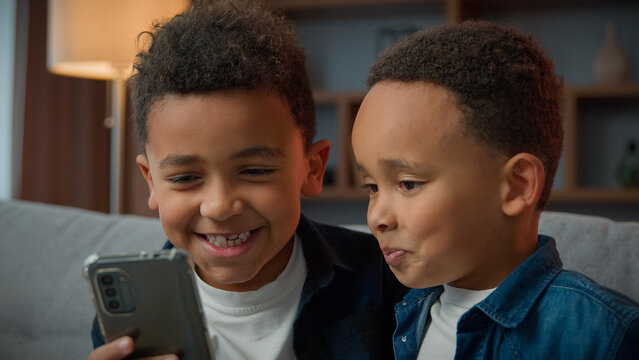 Two African American little boys brothers laughing browsing mobile phone without parents bad behavior young generation children and modern technology addicted kids siblings using funny smartphone app