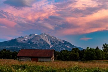 Barn structure in the center of a vast meadow under a sunset near Mt Sopris in Carbondale, Colorado