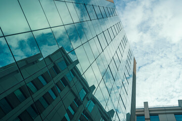 Glass facade of modern building reflecting another building with blue sky with white clouds.