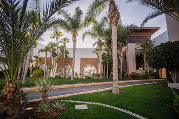 Agadir, Morocco - February 25, 2024 - Tropical garden with palm trees, cacti, and a curved walkway in a resort setting.