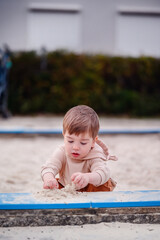 Intently focused, a young child plays in a sandbox, his hands busy sculpting sand, lost in the...