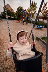 A child's laughter fills the air as they swing joyfully at the playground, dressed in a whimsical bear costume, embodying the innocence and playfulness of youth