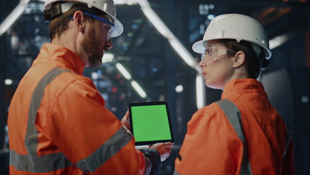 Factory boss showing green screen tablet to woman employee in facility close up.