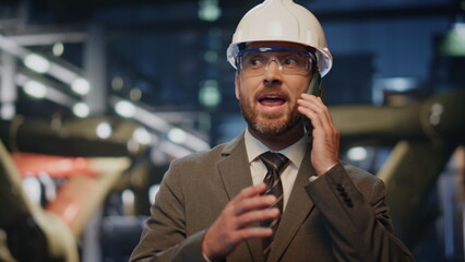 Factory engineer speaking cellphone at production in protective helmet close up.