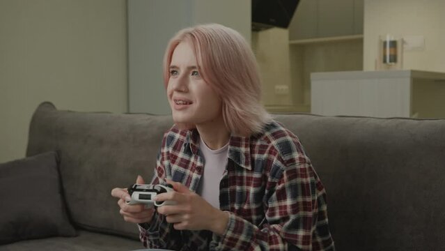Exited Woman Playing Video Game Holding Joystick. 20s female winning video game sitting on couch at home. Happy with game victory. 4K