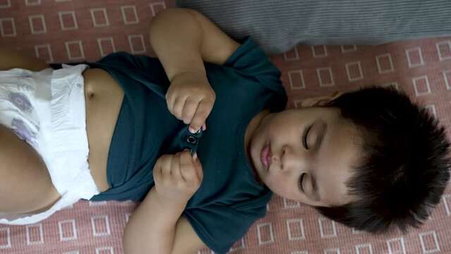Toddler getting nappy change on a checkered mat, playing with shirt button, overhead shot