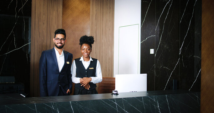 Portrait of polite, professional male and female workers of fancy hotel in uniform. Indian and African-American hotel managers smiling and looking into the camera. Customer care concept.