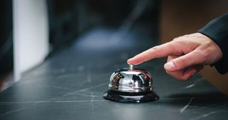 Close-up of elegant businessman ringing bell at front desk. Visitor and professional receptionist....