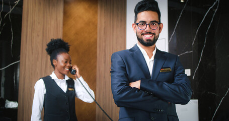 Portrait of handsome happy luxury hotel receptionist in suit looking at camera and smiling....