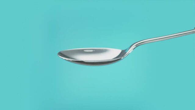Empty metal teaspoon turning to the side to spill out the contents. Cut out on blue screen