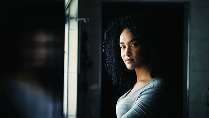 Happy Portrait of a young black Brazilian woman turning head to camera smiling standing by window...