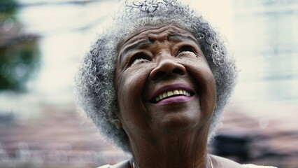 Hopeful Senior African American woman gazing up at sky during drizzle rain having FAITH and HOPE. One gray hair black lady turning head upwards