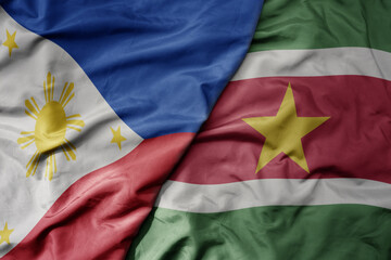 big waving national colorful flag of suriname and national flag of philippines.