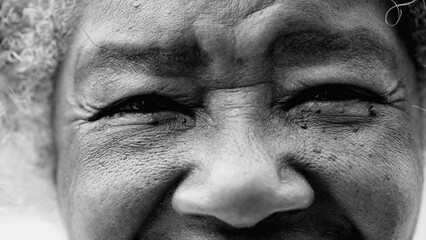 Macro closeup of a wrinkled black senior woman eyes looking at camera depicting old age and wisdom in black and white. African American detail face