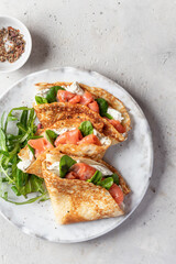 Crepes or thin pancakes with smoked salmon, soft cheese and spinach on a plate top view close up on...