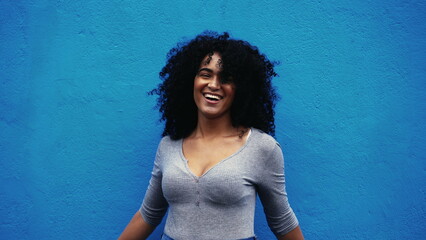One hapyp young black Brazilian woman authentic real life laugh and smile standing in outdoor blue...