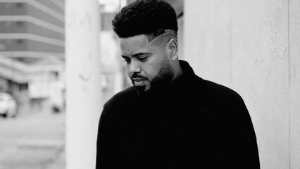 One introspective young black man with deep pensive emotion standing in street gazing solemnly to...