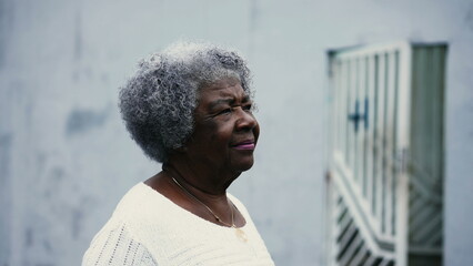 One pensive black senior woman strolling outdoors in city street with thoughtful gaze, close-up...