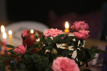 Rosa Rosen auf eiem Tisch und im Hintergrund eine brennende kerze