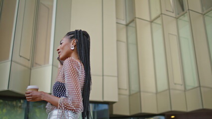 Closeup trendy girl talking phone hold tea at city. Dreadlocks woman walking