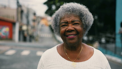 One happy black senior woman walking forward to camera in urban setting stret. Gray hair elderly South American lady in 80s depicting active mature old age, portrait close-up