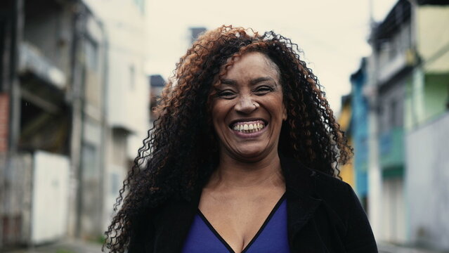 One happy middle aged Brazilian black woman smiling and laughing while walking forward toward camera in urban city street environment, authentic real life laugh and smile