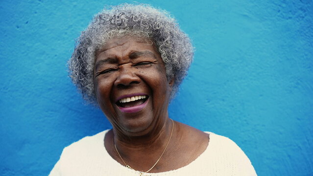 One happy senior African American elderly woman with gray hair laughing and smiling in blue wall backdrop. Portrait a joyful latin older person