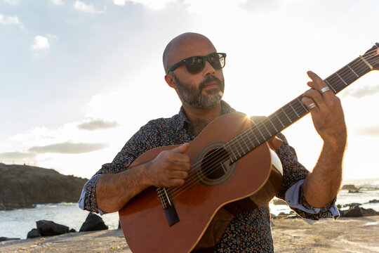 Man playing guitar by the sea at sunset