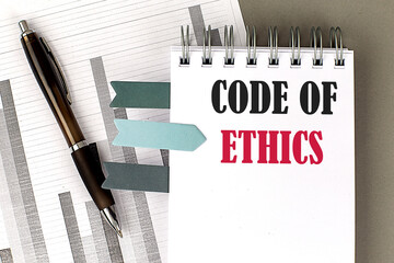 CODE OF ETHICS text on notebook with pen, calculator and chart on a grey background