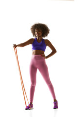 Young athletic African-American woman doing exercises with gym band against white studio background. Training. Concept of sport, mourning routine, active and healthy lifestyle, energy, action.