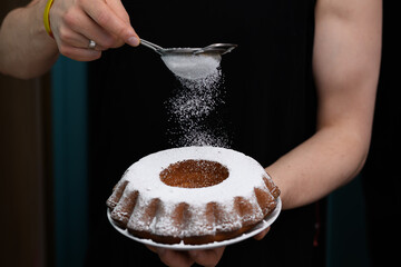 Mężczyzna trzyma talerz z ciastem wielkanocnym i posypuje je cukrem pudrem 