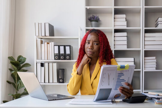 African American businesswoman is unhappy sitting on her office desk doing accounting and finance work.