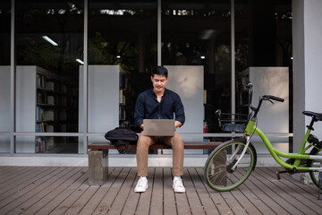 A young Asian businessman rides a bicycle to work. Use a reusable water bottle. Working outside of the office using a laptop The concept of saving energy and reducing pollution to the environment.