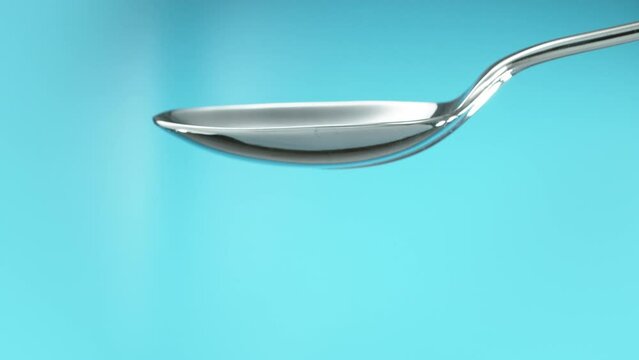 Empty metal teaspoon turning to the side to spill out the contents. Cut out on blue screen