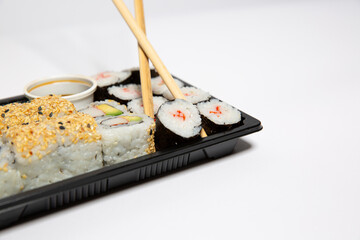 Sushi to go in a black takeaway box with wooden chopsticks on white background 