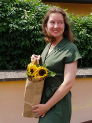 Fototapeta premium A smiling summer girl with a paper bag and sunflowers in her hand.