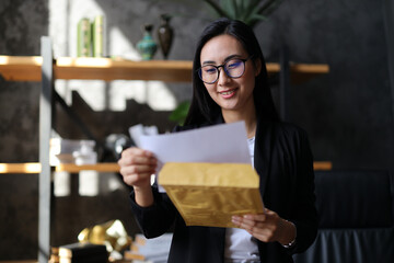 An entrepreneur, Asian woman reads a letter in a cozy office, radiating positivity and determination.